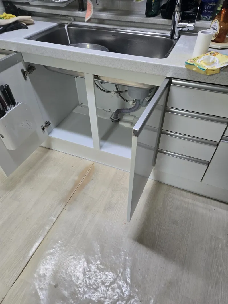 물기가 남은 바닥과 열려 있는 싱크대 하부장